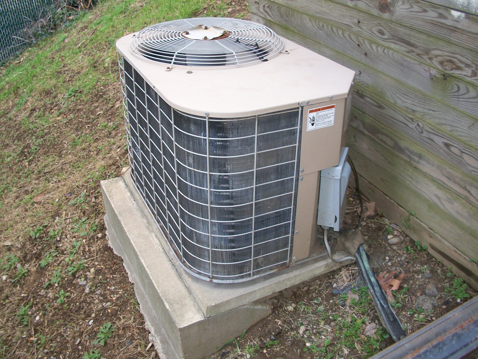 Residential air conditioning condenser on a concrete pad beside a fence